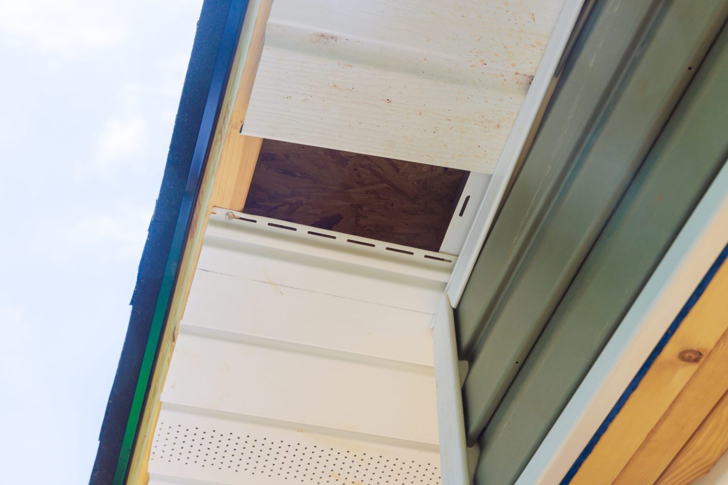 Installation of vinyl soffit plastic panels on facade ceiling new house by an employee